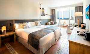 Hotellrom med to senger, nattbord, sittegruppe og balkong med havutsikt. (AI-generert tekst)