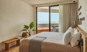 Et lyst og moderne innredet hotellrom med en stor seng og en balkong med utsikt over havet. (AI-generert tekst)