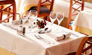 Et dekket bord med hvite duker, glass, bestikk, servietter og en liten blomsterdekorasjon. (AI-generert tekst)