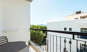 Balkong med bord og stoler, utsikt mot grøntområde og nærliggende bygninger. (AI-generert tekst)