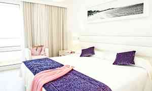 Et lyst hotellrom med en dobbeltseng og dekor i lilla og hvitt. (AI-generert tekst)