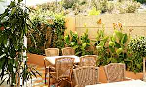 Utemøbler med bord og stoler i rotting foran en frodig hage. (AI-generert tekst)