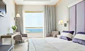 Et hotellrom med moderne innredning. Sengen er oppredd med hvite og lilla puter, og et stort vindu med utsikt over havet er synlig. (AI-generert tekst)