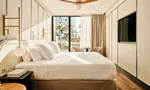 Et moderne hotellrom med en stor seng, to stoler foran vinduet og en takvifte. (AI-generert tekst)