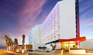 Moderne hotell med opplyste palmer ved hovedinngangen og en fargerik fasade. (AI-generert tekst)