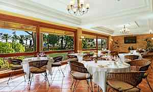 En elegant restaurant med dekkede bord og flettede stoler. Store vinduer gir utsikt over en hage. (AI-generert tekst)