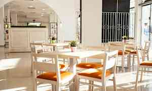 Lyse tremøbler med oransje sittepute i et solfylt rom med store vinduer. (AI-generert tekst)