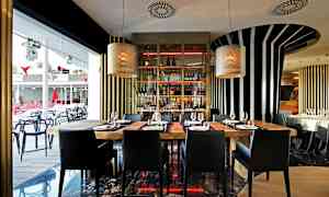 Interiør av en moderne restaurant med trebord og svarte stoler, omgitt av stripete veggdekorasjoner og store vinduer. (AI-generert tekst)