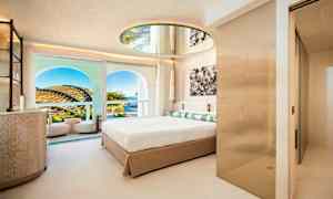 Et moderne hotellrom med en stor seng, et rundt speil i taket og en balkong med utsikt over landskapet og himmelen. (AI-generert tekst)