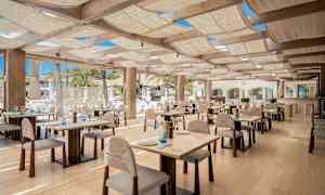 En restaurant med trebord og stoler, godt opplyst med naturlig lys. (AI-generert tekst)