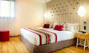 Et soverom med en stor seng, pynteputer og et fargematchende sengeteppe. På veggen bak sengen finnes dekorative detaljer, og til høyre står et nattbord. (AI-generert tekst)