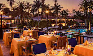 Utendørs servering med dekkede bord, omgitt av palmer ved et basseng i skumringen. (AI-generert tekst)