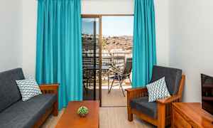 Stue med mørke møbler, blå gardiner og utsikt fra balkong. (AI-generert tekst)