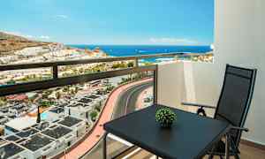 Utsikt fra en balkong mot havet, med et bord og en stol. (AI-generert tekst)