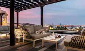 Moderne sittegruppe på terrasse med utsikt over havn og by i skumringen. (AI-generert tekst)