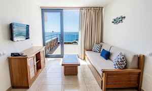 Et hotellrom med sittegruppe og utsikt mot havet fra en balkong. (AI-generert tekst)