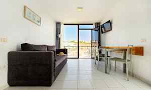 En stue med en mørk sofa, et spisebord med stoler og en balkong med utsikt. (AI-generert tekst)