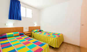 Et rom med to enkeltsenger dekket med fargerike mønstrede sengetepper. (AI-generert tekst)