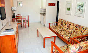 En stue med en sofa med blomstrete tekstil, et sofabord, en kjøkkenkrok og en spiseplass med stoler. (AI-generert tekst)