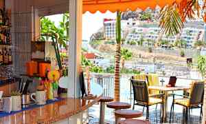 En kafé med utsikt over en solrik vei og bygninger. (AI-generert tekst)