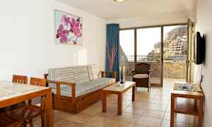 Et stue med treinnredning og utsikt mot en balkong samt bygninger og fjell. (AI-generert tekst)