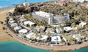 Flyfoto av en kystby med hotell, palmer og strand. (AI-generert tekst)