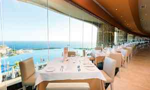 En restaurant med dekkede bord og utsikt over havet gjennom store glassvinduer. (AI-generert tekst)