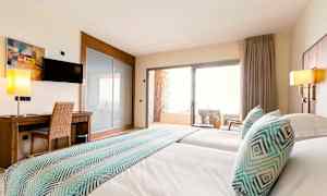 Bilde av et hotellrom med to senger, en skrivebordsplass, en TV og en balkong med stoler. (AI-generert tekst)