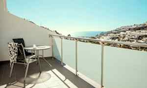 Balkong med bord og stol, utsikt mot havet og bebyggelse. (AI-generert tekst)