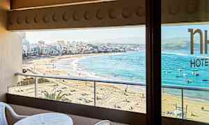 Utsikt fra en balkong mot en sandstrand og by med klart blått hav. (AI-generert tekst)