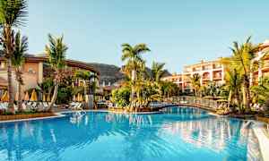 Bassengområde med parasoller og palmer ved et hotell. (AI-generert tekst)