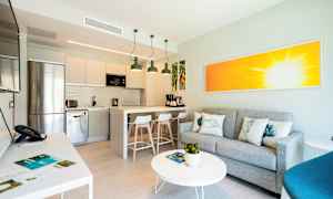 Interiør av et moderne kjøkken med integrert stueområde, grå sofa og fargerikt kunstverk. (AI-generert tekst)