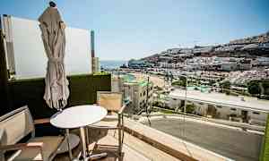 Balkong med utsikt over en strand og fjell dekket med bygninger. (AI-generert tekst)