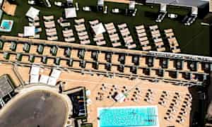 Luftfoto av hotellområde med basseng, solsenger og parasoller. (AI-generert tekst)