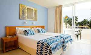 Et hotellrom med to enkeltsenger, en blå vegg og en glassdør som leder ut til balkongen. (AI-generert tekst)