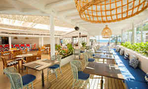 En åpen restaurant med bord og stoler og utsikt mot havet. (AI-generert tekst)