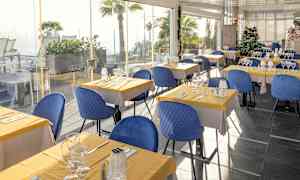 Restaurant med bord dekket med gule duker og blå stoler. (AI-generert tekst)