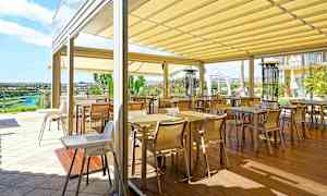 En terrasse med flere bord og stoler under en takmarkise. (AI-generert tekst)