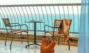 Utsikt over havet fra en balkong med bord, to stoler og en strandveske. (AI-generert tekst)