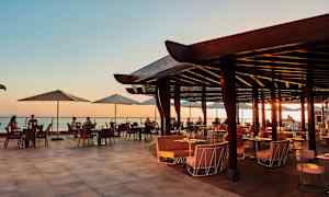 Åpen restaurantterrasse med utsikt over havet ved solnedgang. (AI-generert tekst)