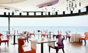 Lyst restaurant med fargerike stoler og utsikt over havet. (AI-generert tekst)