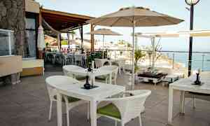 En terrasse med bord og stoler samt utsikt over havet. (AI-generert tekst)