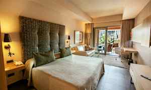 Et hotellrom med en stor seng, sofa og skrivebord. Det er også en balkong med utsikt. (AI-generert tekst)