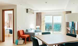 Et hotellrom med sittegruppe, spisebord og havutsikt fra balkongen. (AI-generert tekst)