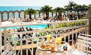 Utsikt fra en balkong med frokostservise mot bassengområde og havet. (AI-generert tekst)