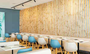 Restaurant med lyse bord og moderne stoler foran en trepanel. (AI-generert tekst)