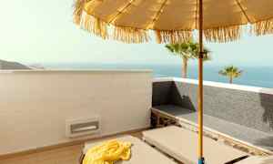 En solseng på en terrasse med utsikt over havet, parasoll og palmer. (AI-generert tekst)