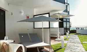 Utendørsvisning med to solsenger og parasoller ved en bygning. (AI-generert tekst)