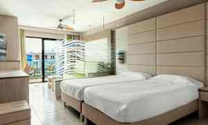 Et hotellrom med to enkeltsenger, en sittegruppe og en balkong med utsikt. (AI-generert tekst)