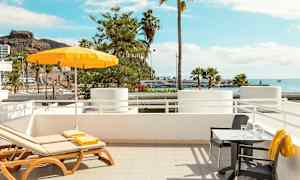 Solstoler og bord med utsikt over havet og palmer. (AI-generert tekst)